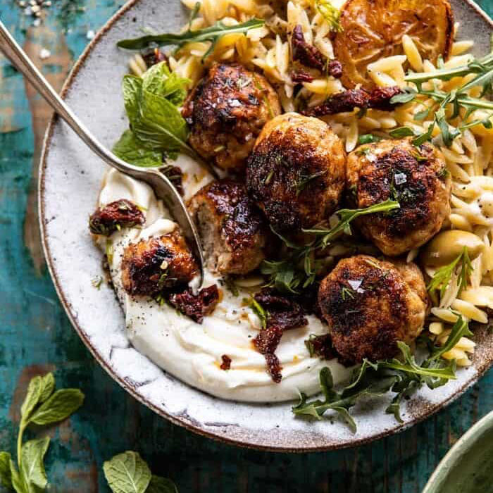 Plated dish with meatballs, pasta, and herbs on a rustic wooden surface